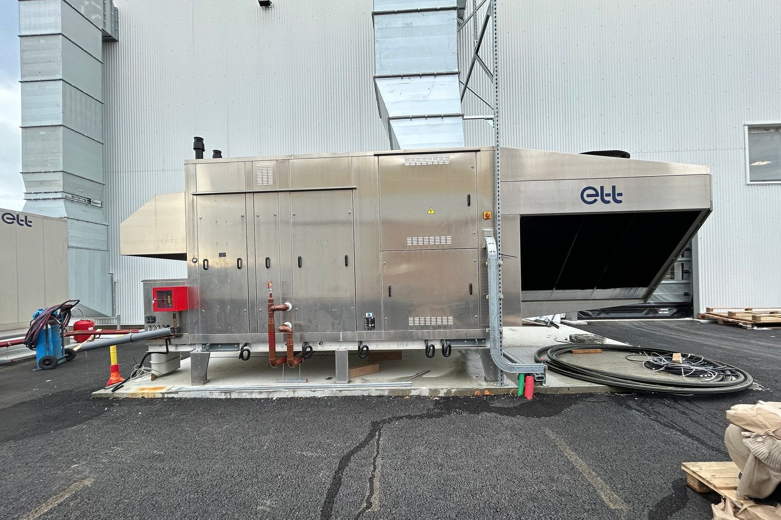 Centrale de traitement d’air en inox au pied de l’atelier Dufour Yachts à Périgny, gaines montant le long de la façade.