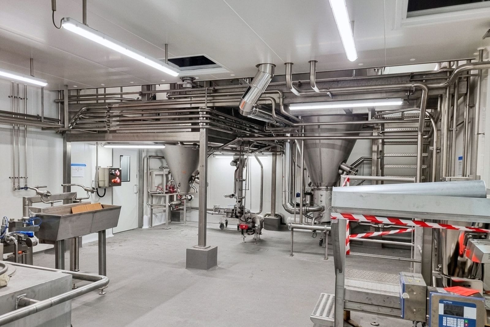 Atelier pilote agroalimentaire tout inox des ateliers Capsulae à La Rochelle : trémies de process et réseaux suspendus sous plafond.