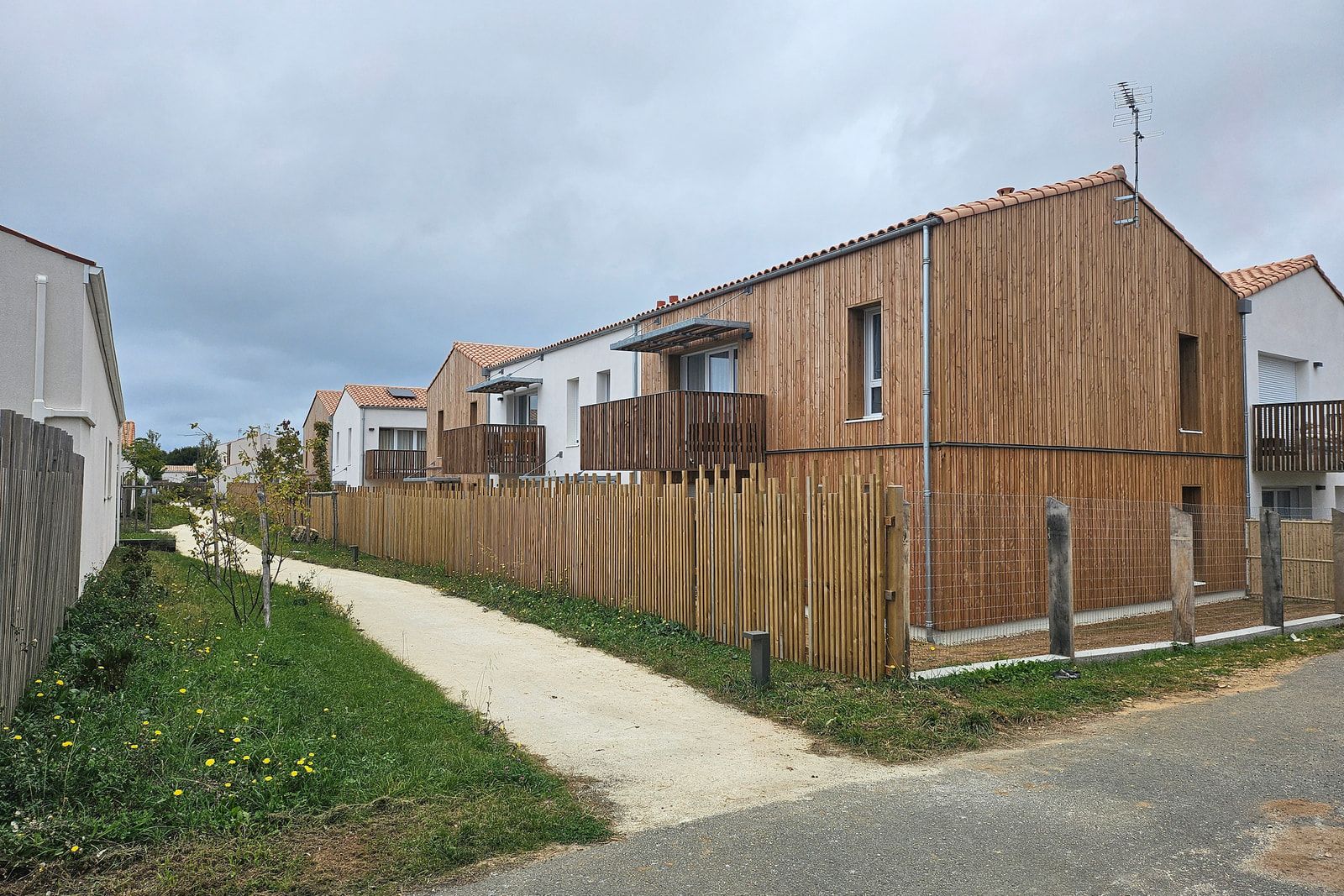 Logements sociaux de l’ÉcoQuartier de L’Houmeau : bardage et balcons bois, clôtures en ganivelles le long d’une allée piétonne.