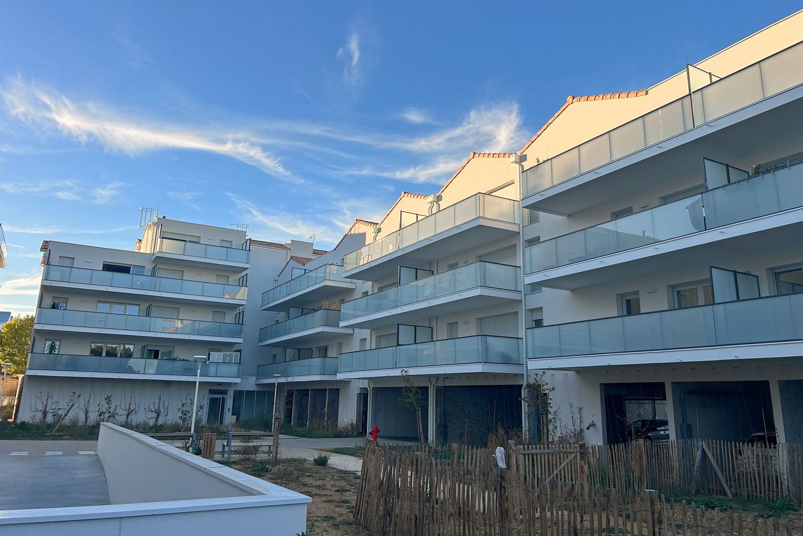 Résidence Néréa à Aytré : bâtiments de logements à balcons filants vitrés autour d’un cœur d’îlot, clôtures en ganivelles.