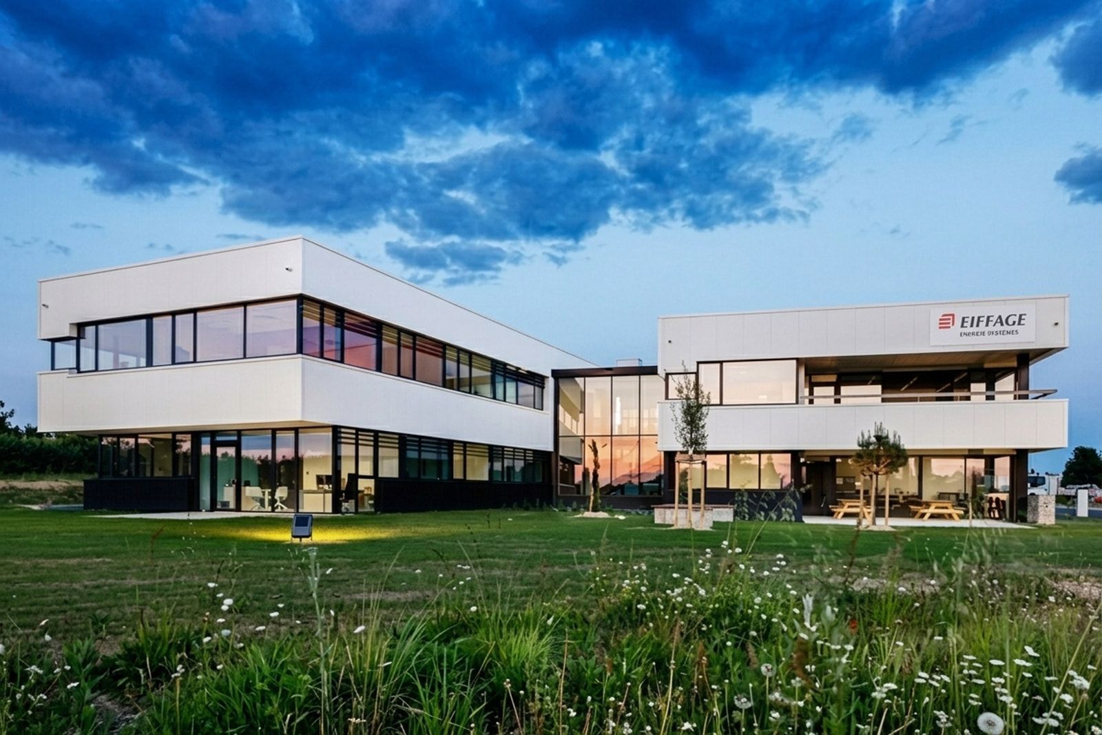 Siège d’Eiffage Énergie Systèmes à Saint-Jean-d’Angély à l’heure bleue : deux ailes de bureaux vitrées reliées par une faille centrale.